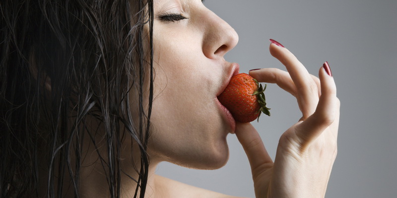 Topless caucasian woman biting a strawberry.